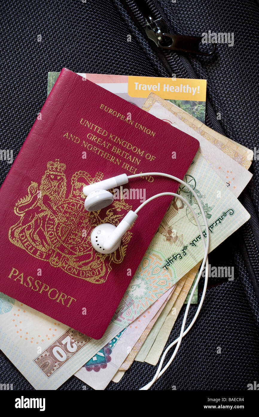 Close up d'un passeport britannique, des devises étrangères, la carte santé de voyage et votre lecteur mp3 casque dans le top d'une valise Banque D'Images