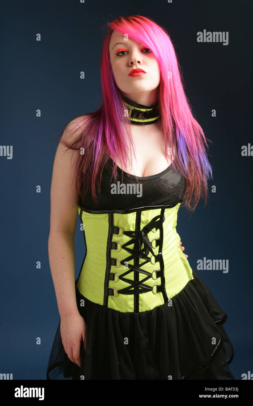 Young teen fille avec des cheveux rose vif, rouge lèvres et peau pâle debout portant un corset et robe noire Banque D'Images