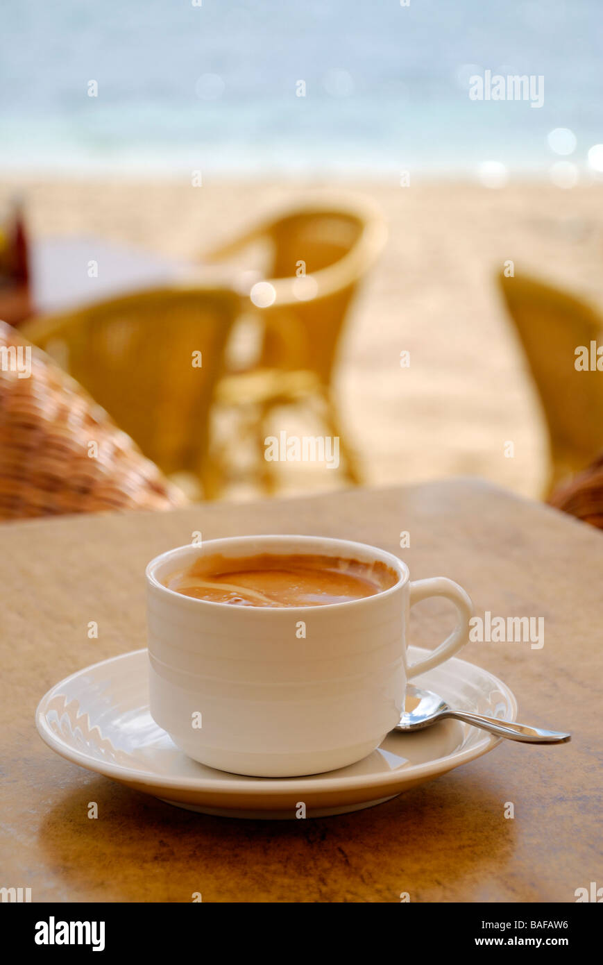 White tasse de café et soucoupe sur la table en bois avec chaises en osier, plage, et la mer en arrière-plan flou Banque D'Images