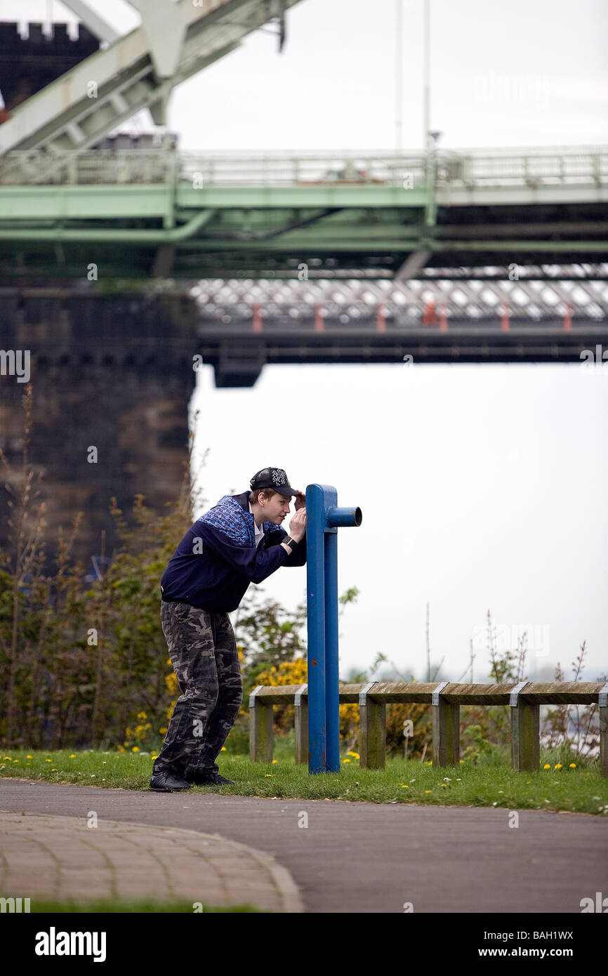 Adolescent solitaire regarde à travers un télescope simulé sur la rivière Mersey à Runcorn, sous le pont du jubilé d'argent Banque D'Images