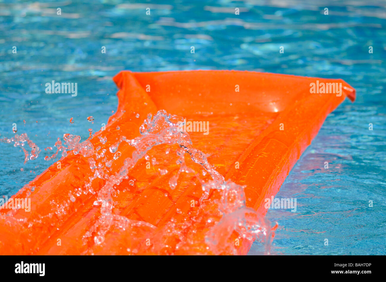 Éclaboussé de l'eau sur un lit d'air orange flottant dans une piscine. Banque D'Images