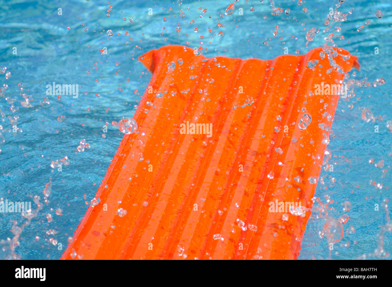 Éclaboussé de l'eau sur un lit d'air orange flottant dans une piscine. Banque D'Images