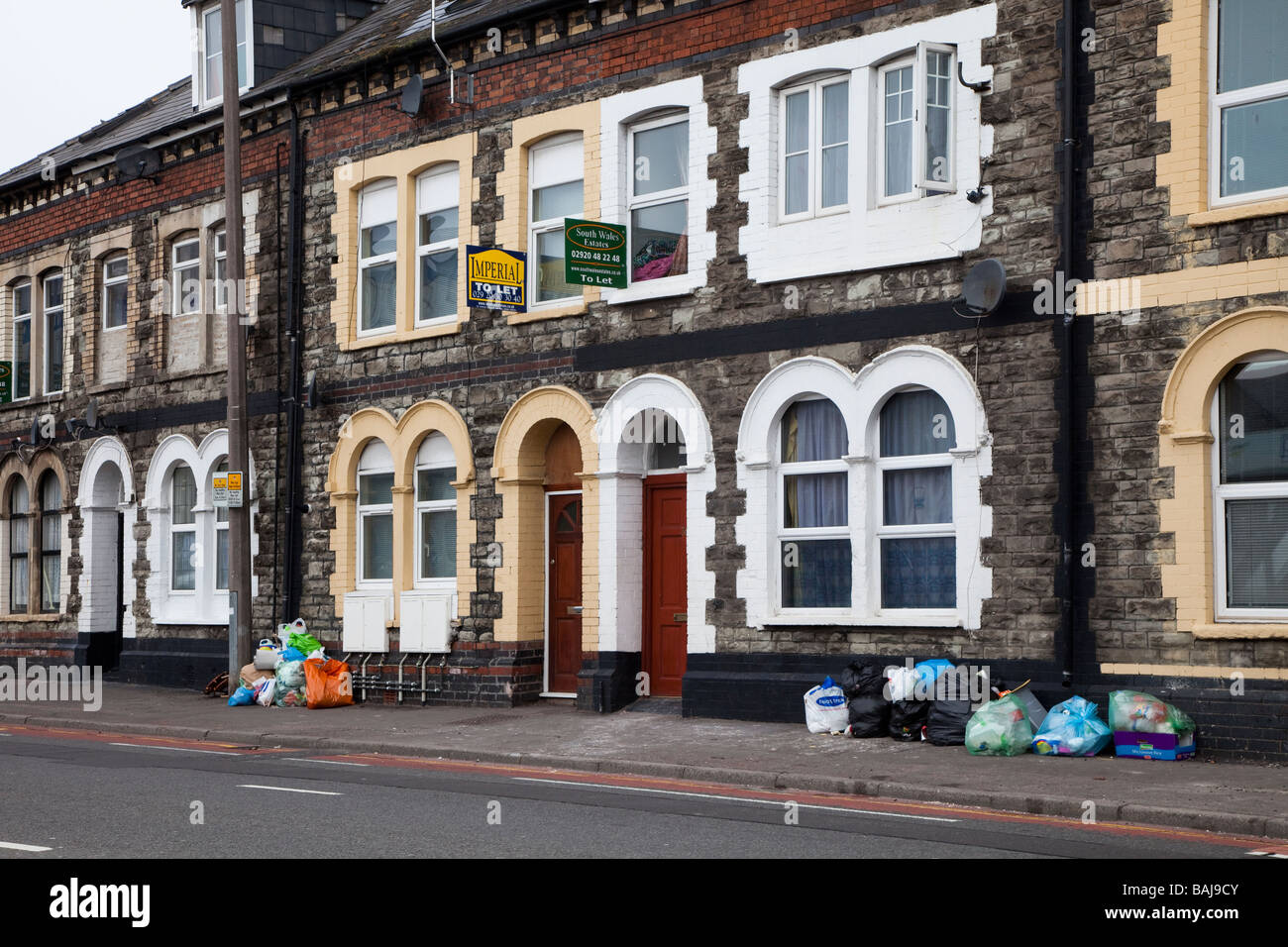 Les ordures dans la rue rangée de maisons mitoyennes avec signes de Cardiff Wales UK Banque D'Images