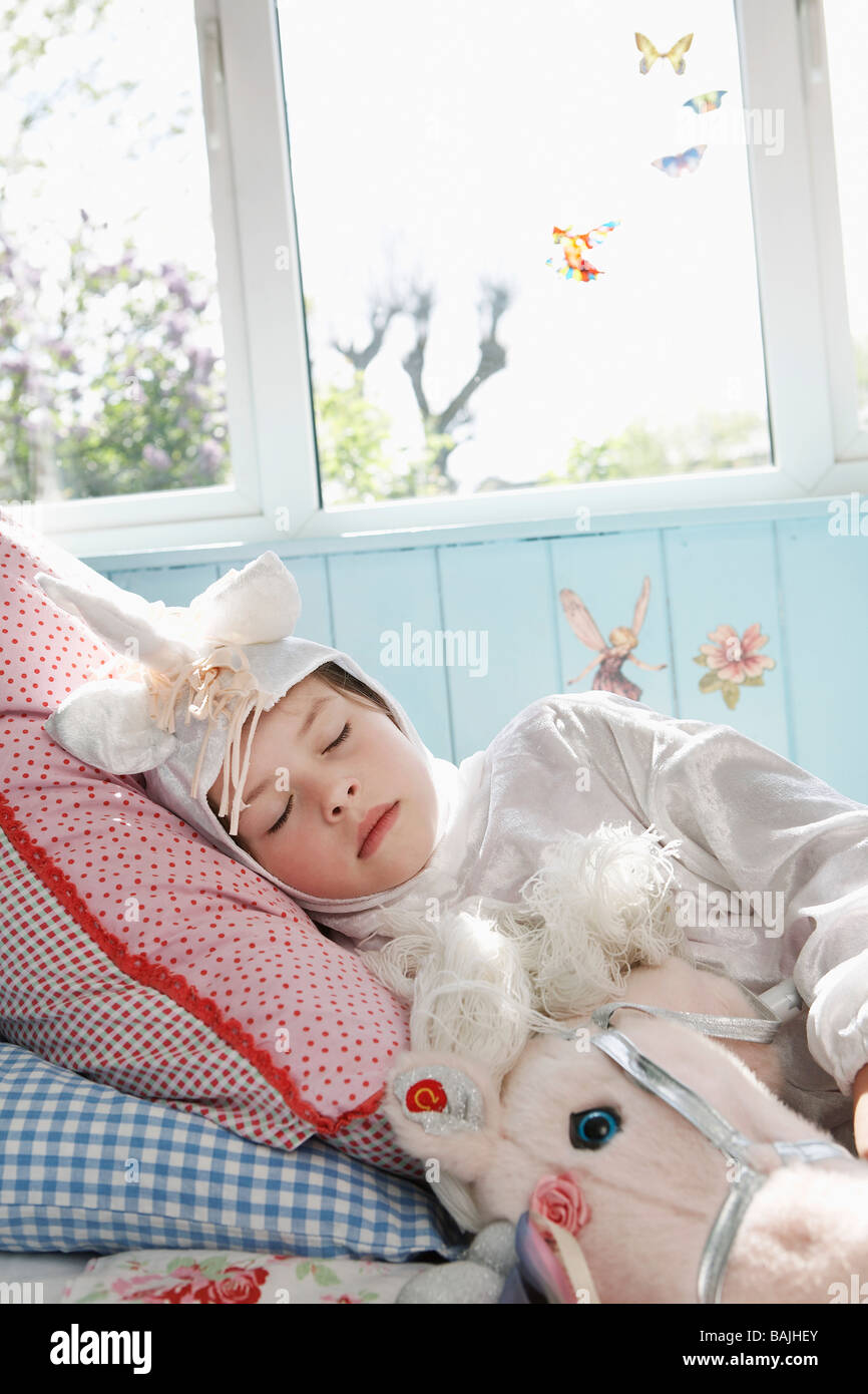 Jeune fille (5-6) en costume de licorne de dormir sur le lit avec cheval jouet Banque D'Images