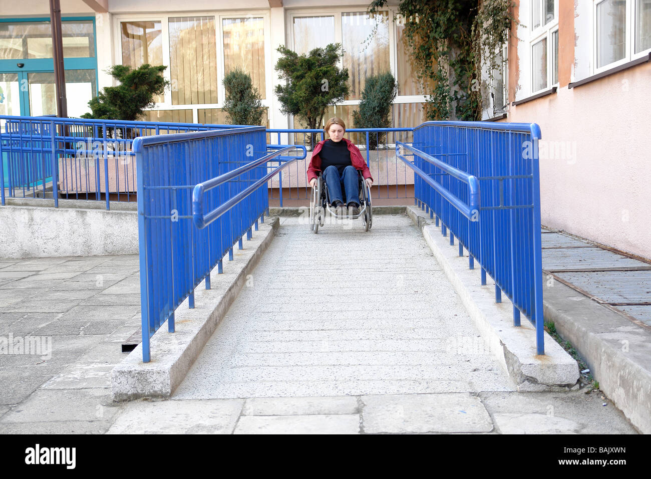 Femme handicapée sur fauteuil roulant quittent l'édifice à l'aide de rampe pour personnes à mobilité réduite Banque D'Images