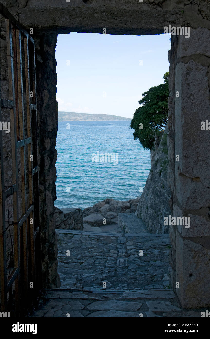 Vue sur la mer par un passage entre les maisons de la vieille ville de Baska, île de Krk, Croatie Banque D'Images