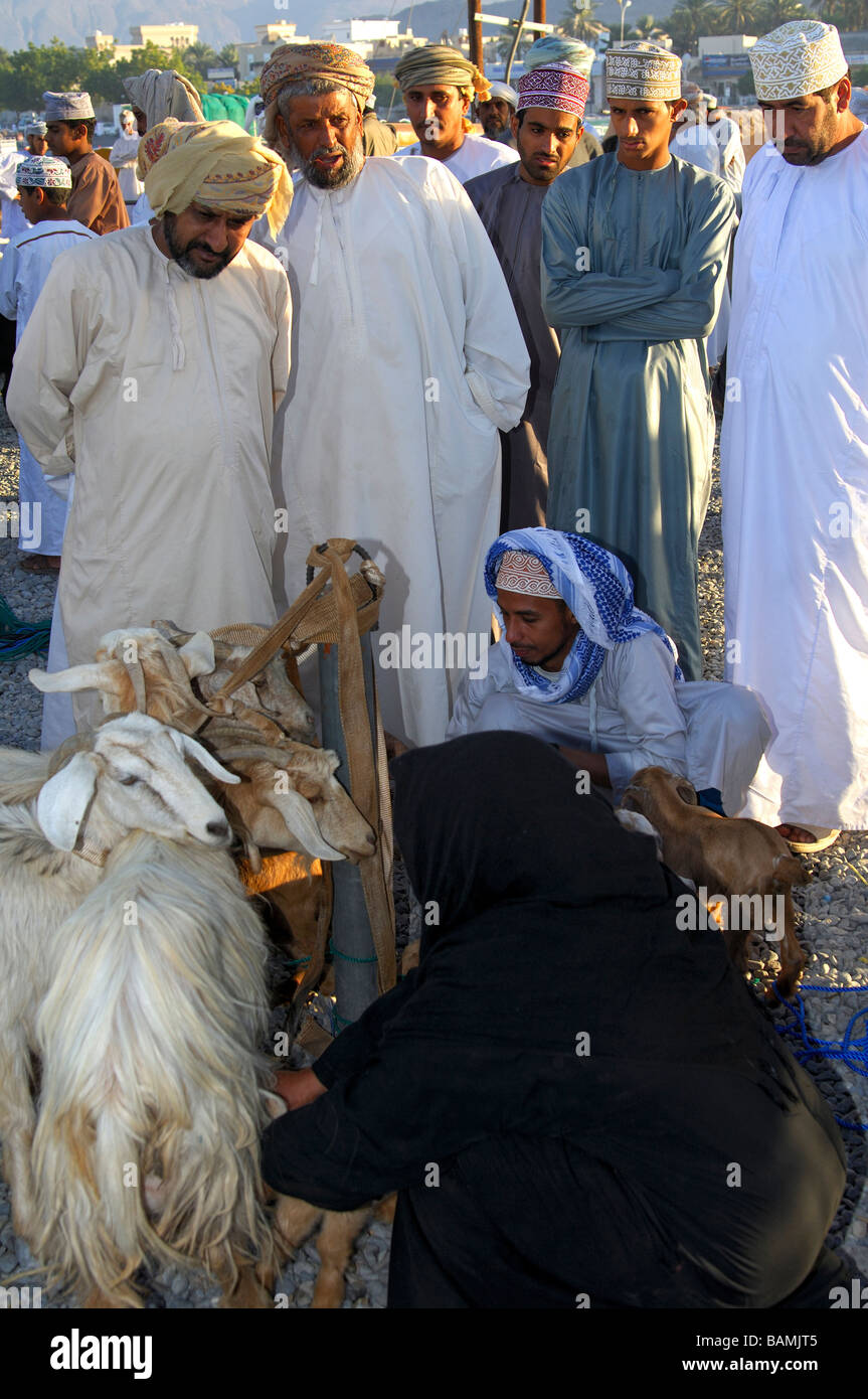 Des gens habillés en costume traditionnel omanais le Dishdasha négociation collective sur le marché de chèvre, Nizwa, Sultanat d'Oman Banque D'Images
