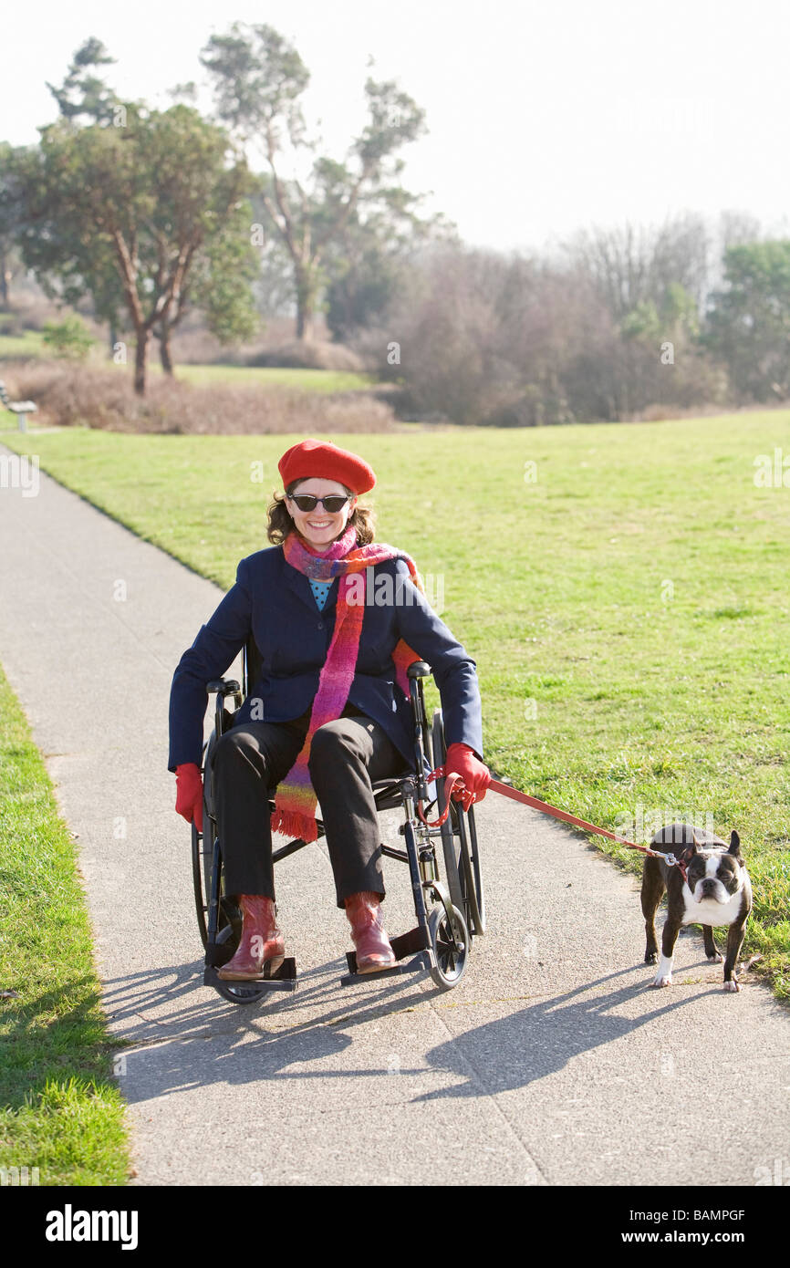 Femme en fauteuil roulant en tenant son chien pour une promenade Banque D'Images