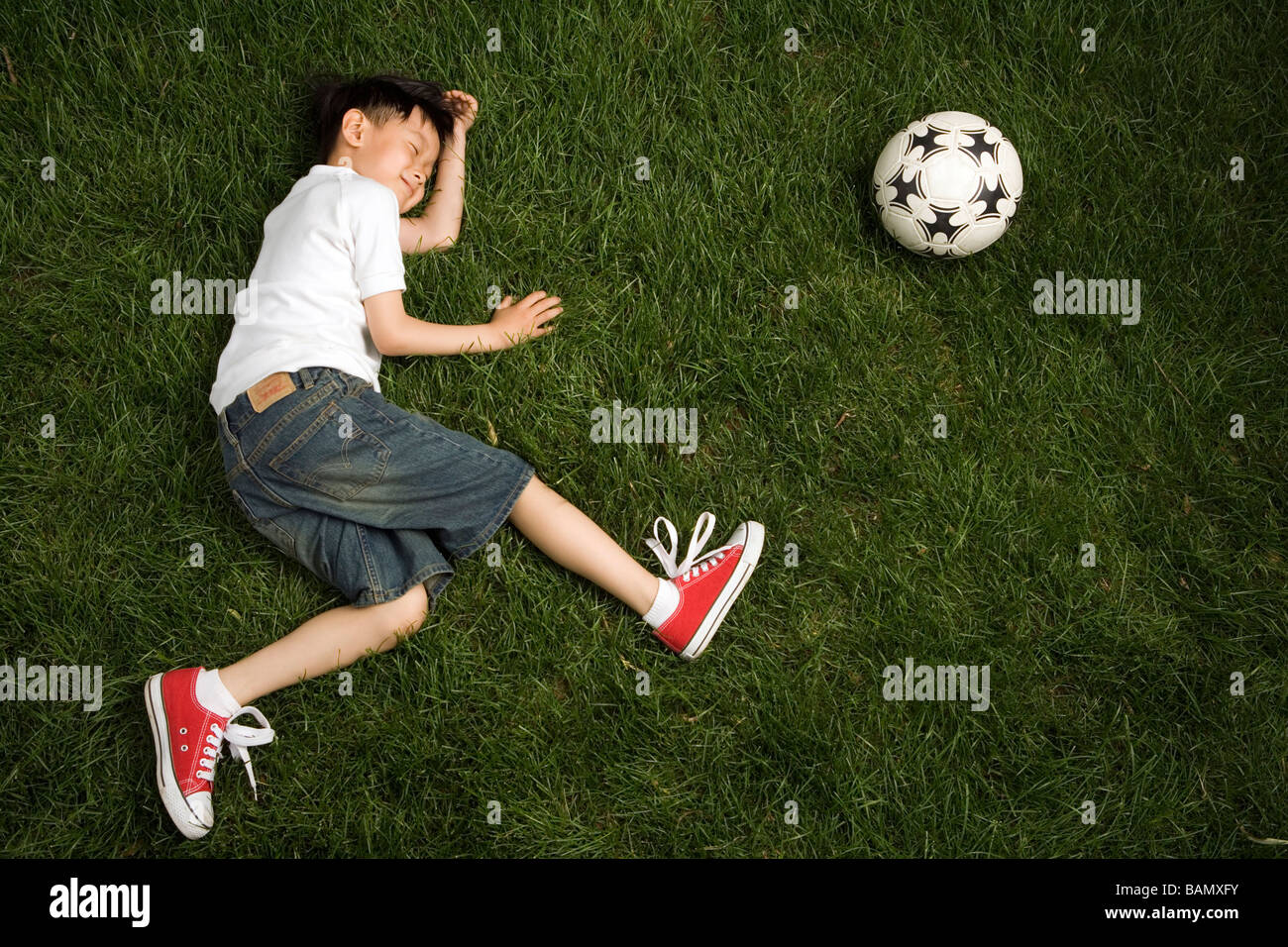 Garçon jouant mort près d'un ballon de football sur l'herbe Banque D'Images