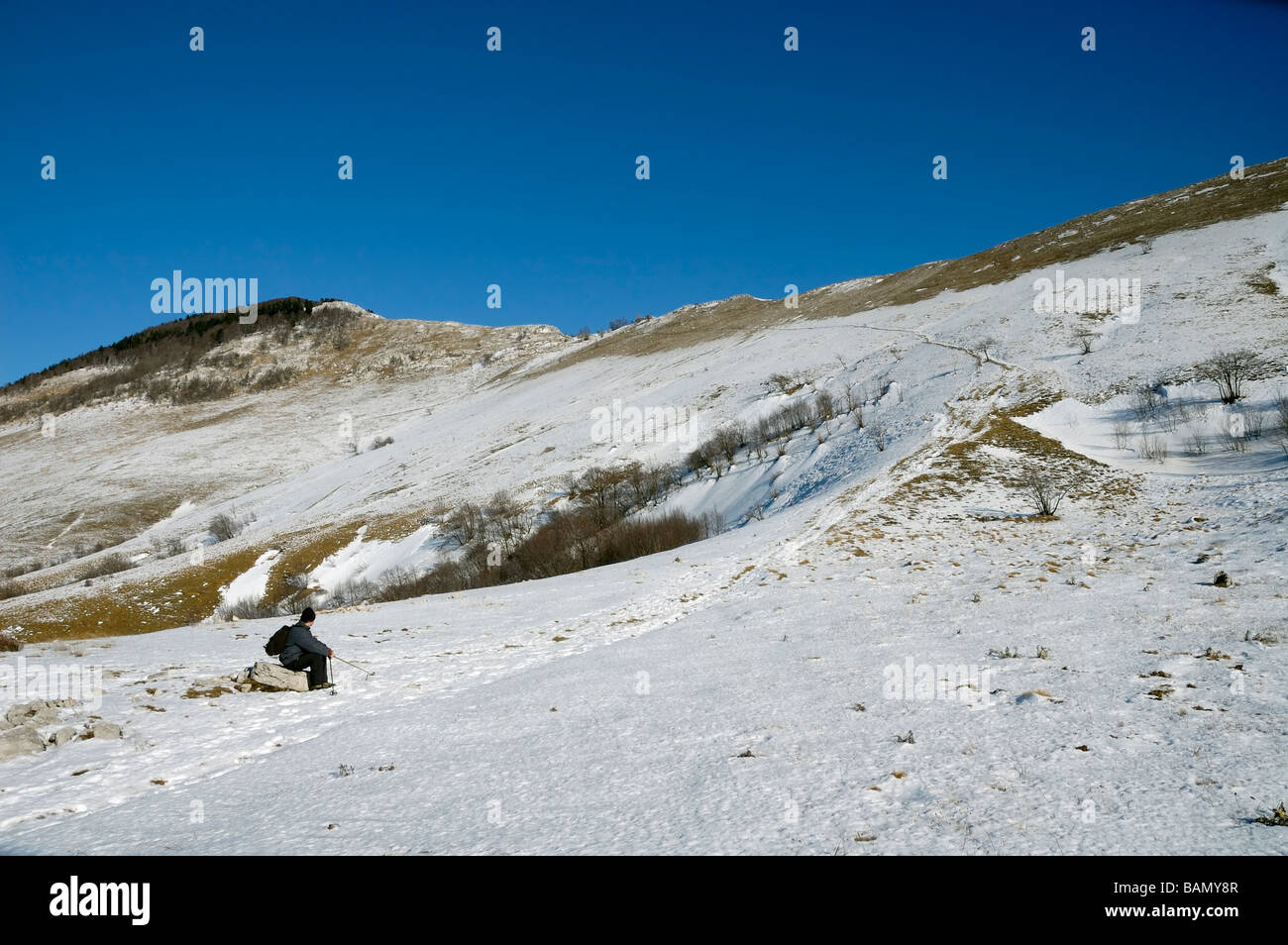 L'alpiniste est assis sur un rocher, le repos sous la montagne couverte de neige pendant la journée ensoleillée Banque D'Images
