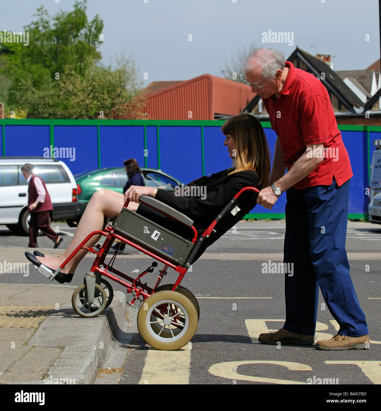 Une manœuvre de soignant masculin style transit fauteuil roulant et à mobilité réduite d'un trottoir en bordure de la femme Banque D'Images