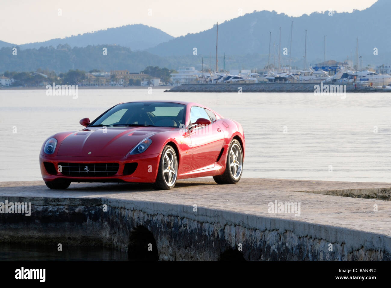 2009 rouge Ferrari sur dock méditerranéenne privée dans la baie de Pollensa au coucher du soleil avec marina et les montagnes en arrière-plan Banque D'Images