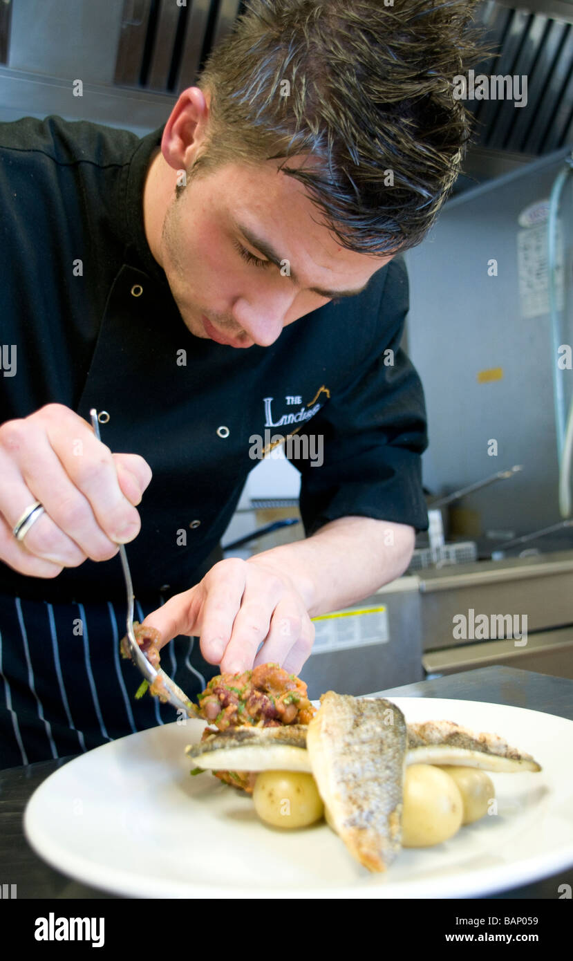 Un chef qui met actuellement la touche finale à un plat de poisson dans la cuisine d'un petit restaurant Banque D'Images