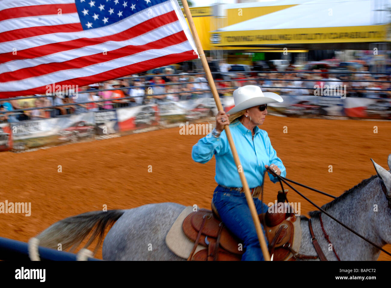 Cowgirl sur les courses de chevaux par la foule dans l'arène de rodéo pendant l'affichage de l'étoile et les bars ou le drapeau de l'United States Banque D'Images