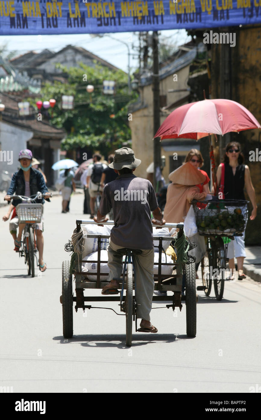 Un vendeur de rue vietnamiens ses cycles de cours le long d'une rue à Hoi An, Vietnam dans le soleil de midi Banque D'Images