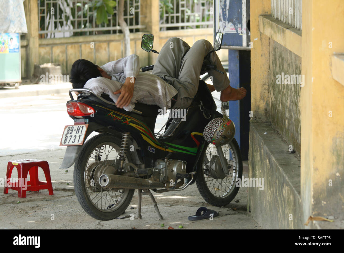 Un homme se détend sur son motrbike dans la chaleur du jour à Hoi An, Vietnam Banque D'Images
