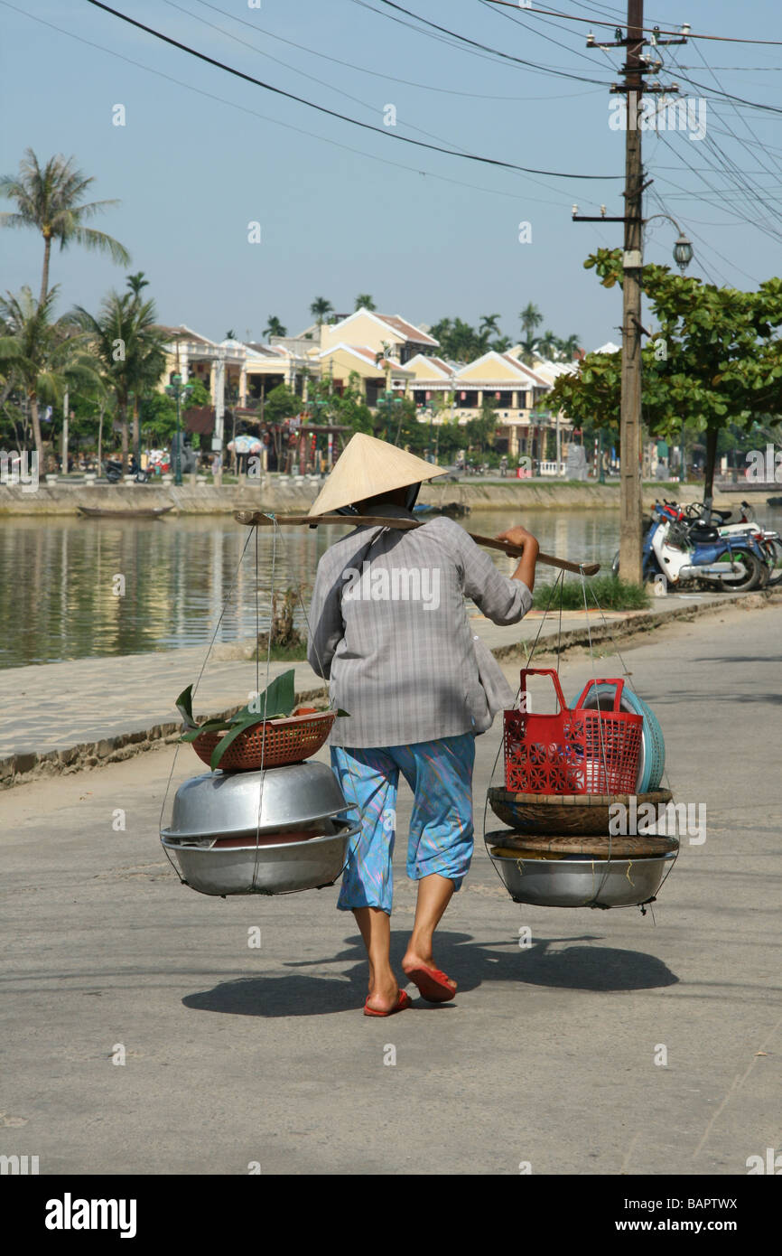 Une femme portant ses marchandises dans la mode traditionnelle vietnamienne à Hoi An, Vietnam Banque D'Images
