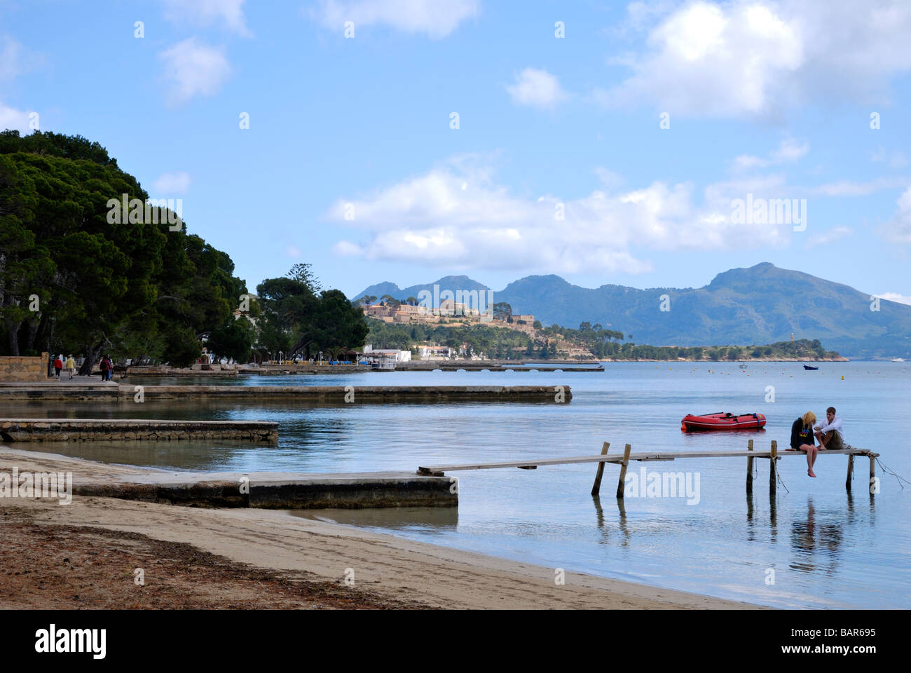 Paysage de la baie de Pollensa et de pin à pied avec un jeune couple sur un quai en bois contre les montagnes et ciel bleu Banque D'Images