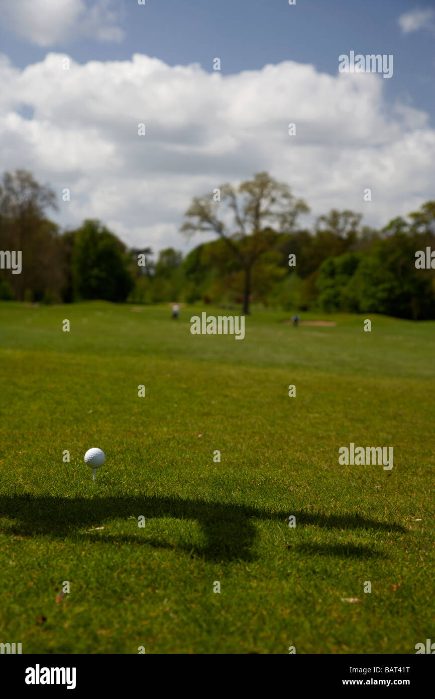 Balle de golf utilisé assis sur le raccord en T avec l'ombre d'un golfeur sur le point de frapper la balle au début d'un parcours de golf Banque D'Images