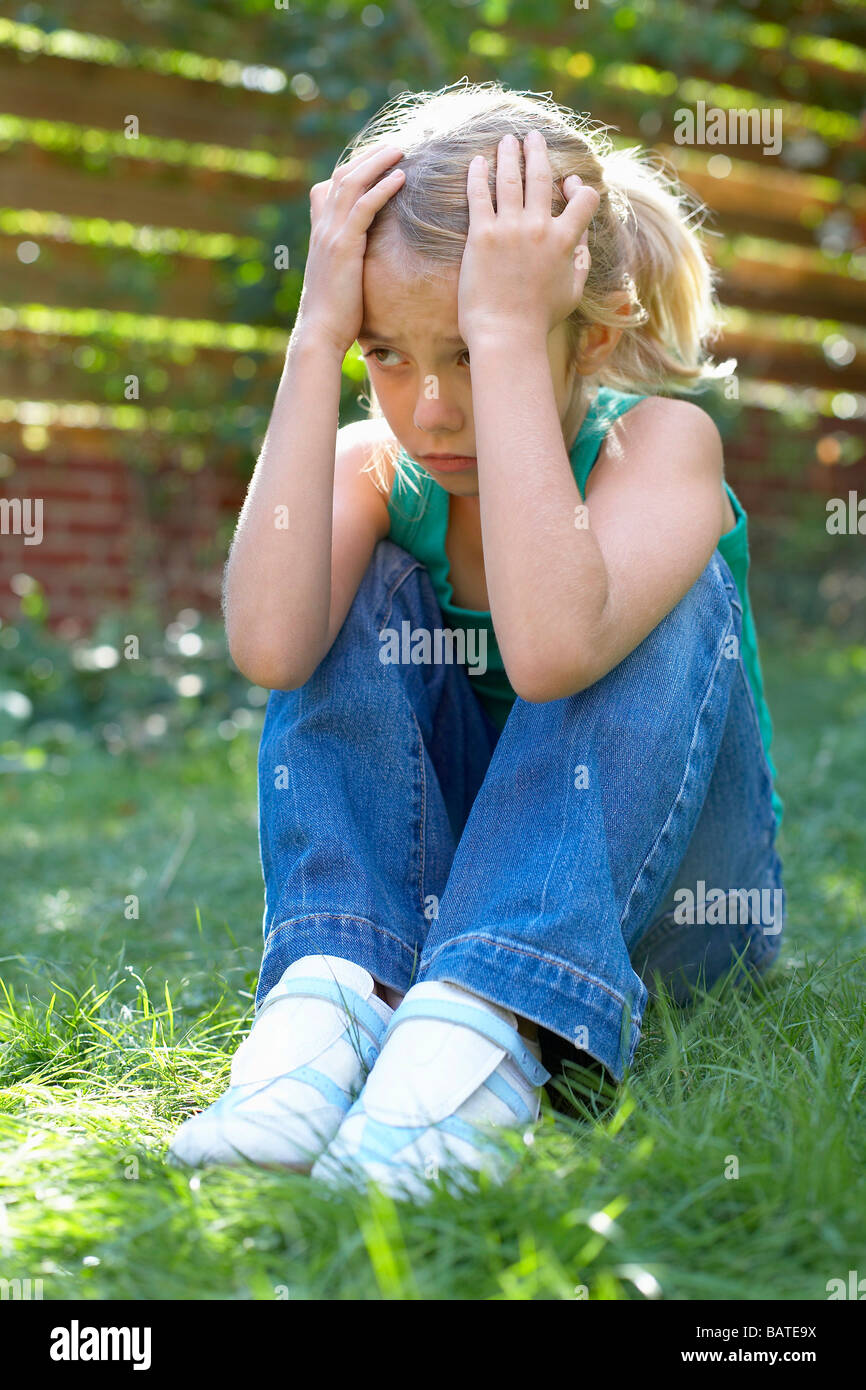 Malheureuse fille assise dans son jardin. Elle a huit ans. Banque D'Images