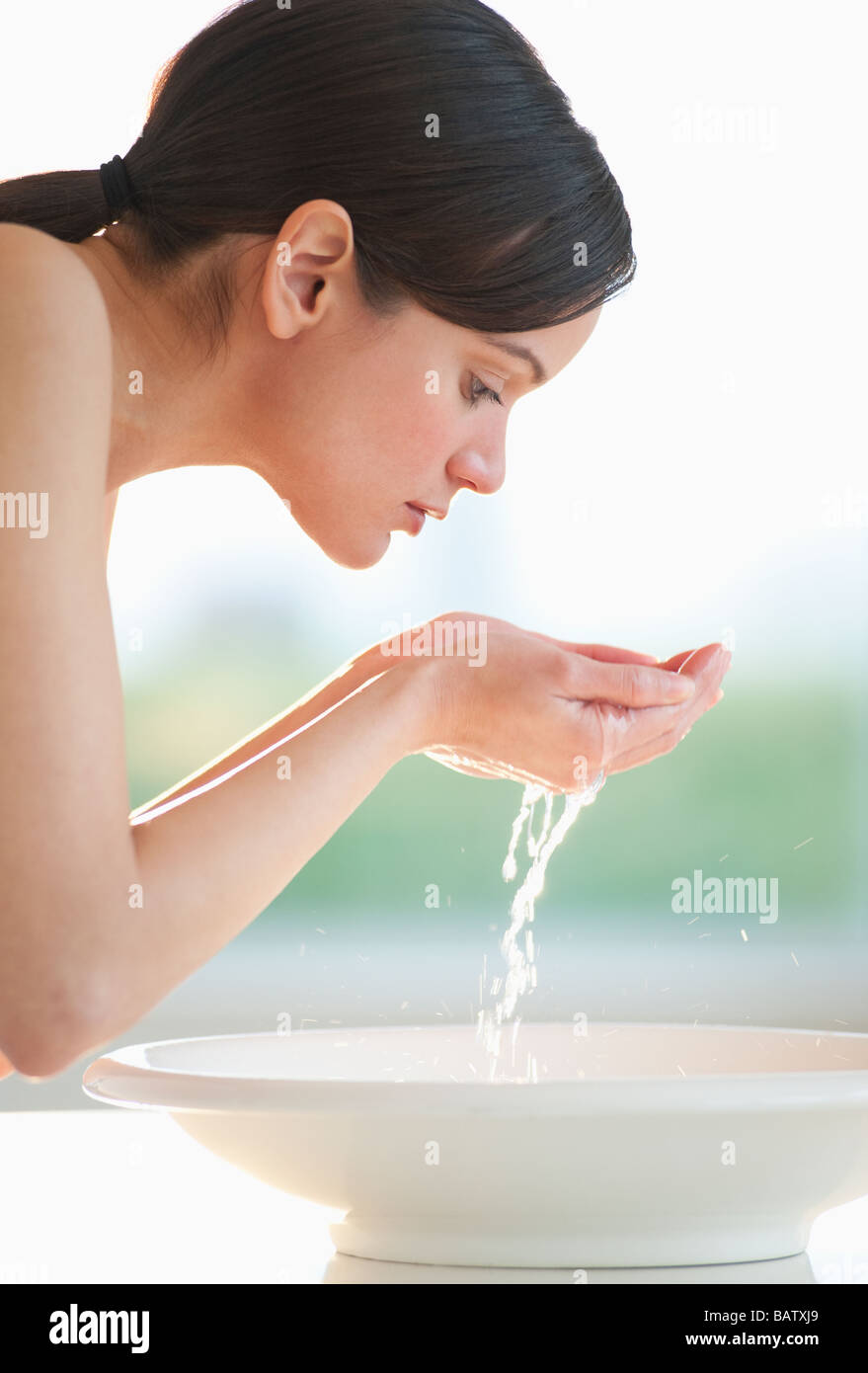 Mid-adult woman lave son visage dans un bol Banque D'Images