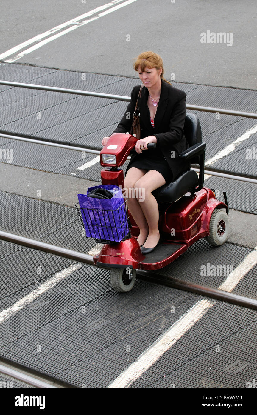 Femme conduire son scooter de mobilité à travers un passage à niveau route England UK Banque D'Images