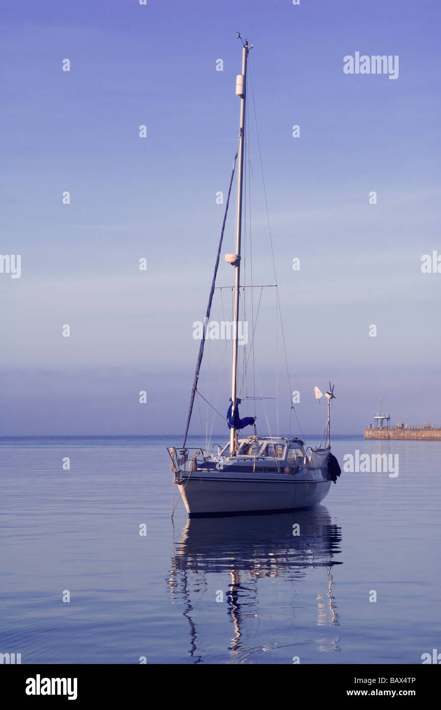 Un yacht solitaire début flottant sur un soir les eaux calmes à l'entrée du port de Weymouth, dans le Dorset, Angleterre. Banque D'Images