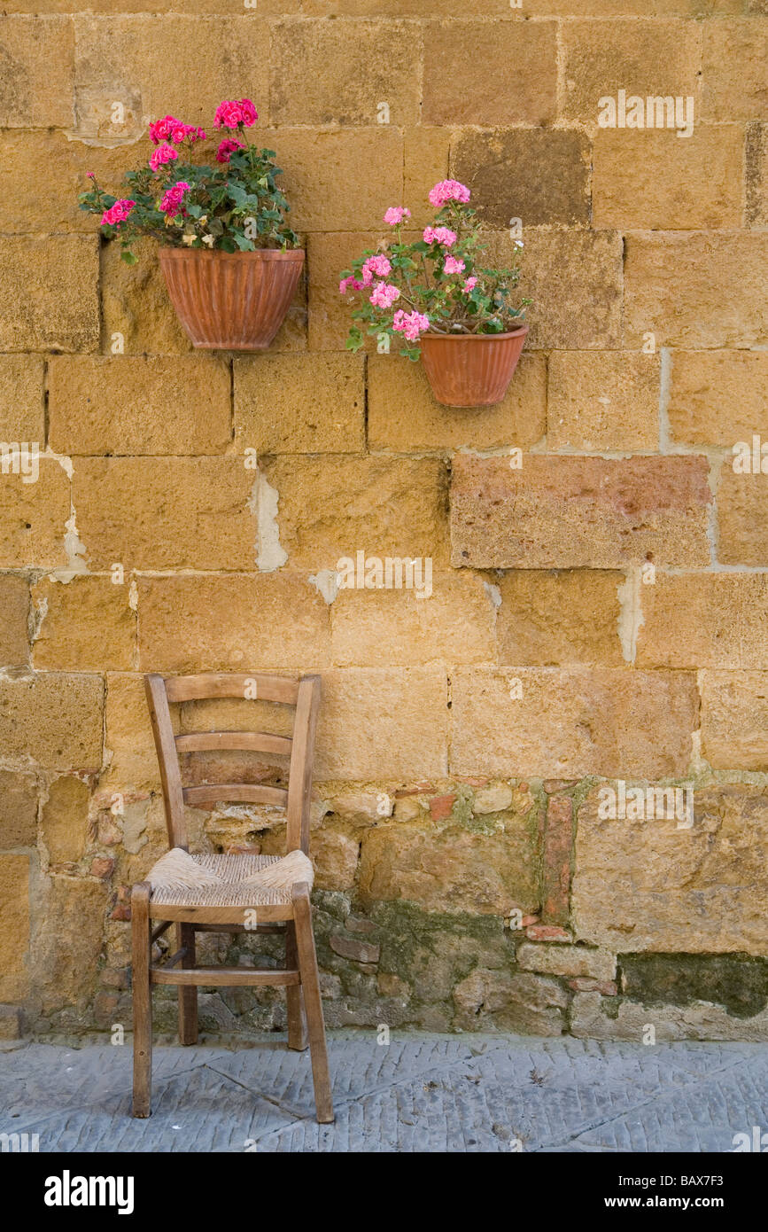 Chaise en bois branlant contre un mur de couleur miel en Toscane avec géraniums en pot Banque D'Images