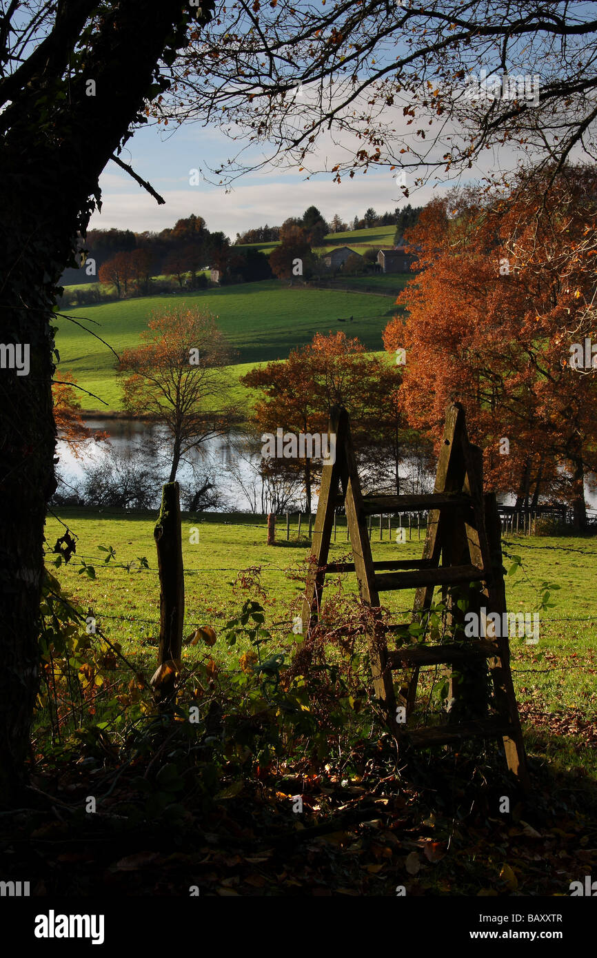 Un vieux stile menant dans un champ. Une rivière et des arbres d'automne derrière. Banque D'Images