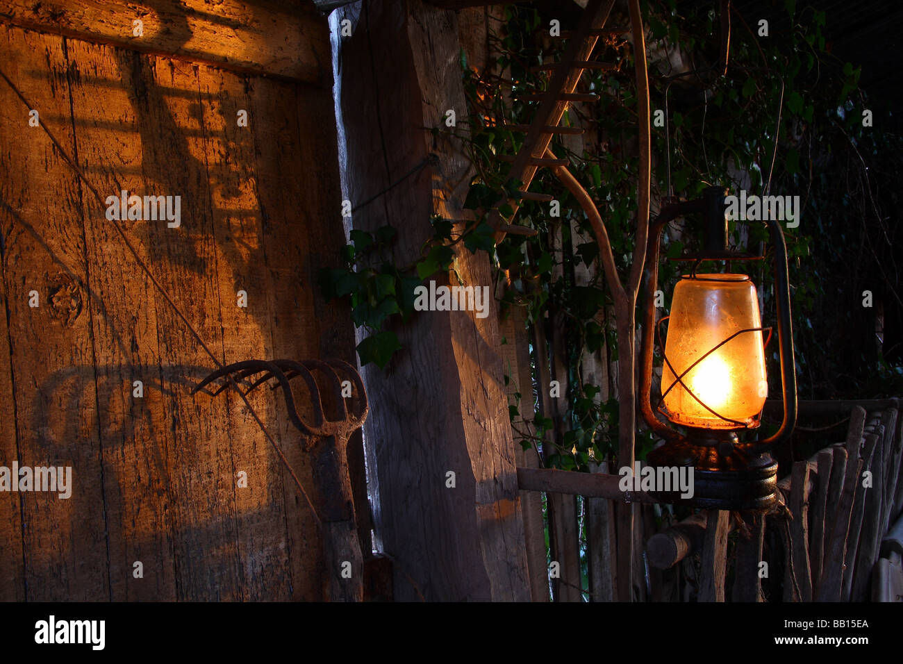 Détail d'une vieille grange en France avec une lampe à huile rouillée et des râteaux et des fourches empilés contre le mur. Banque D'Images