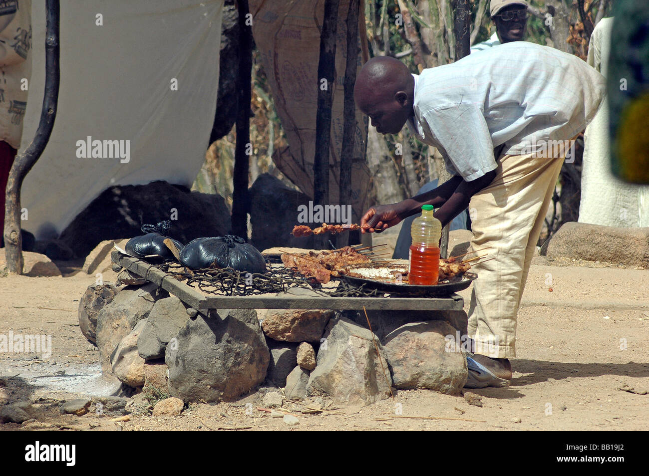 Cameroun, Rhumsiki. Un garçon se plie pour définir des brochettes de viande sur un feu de cuisson traditionnelle. (RF) Banque D'Images