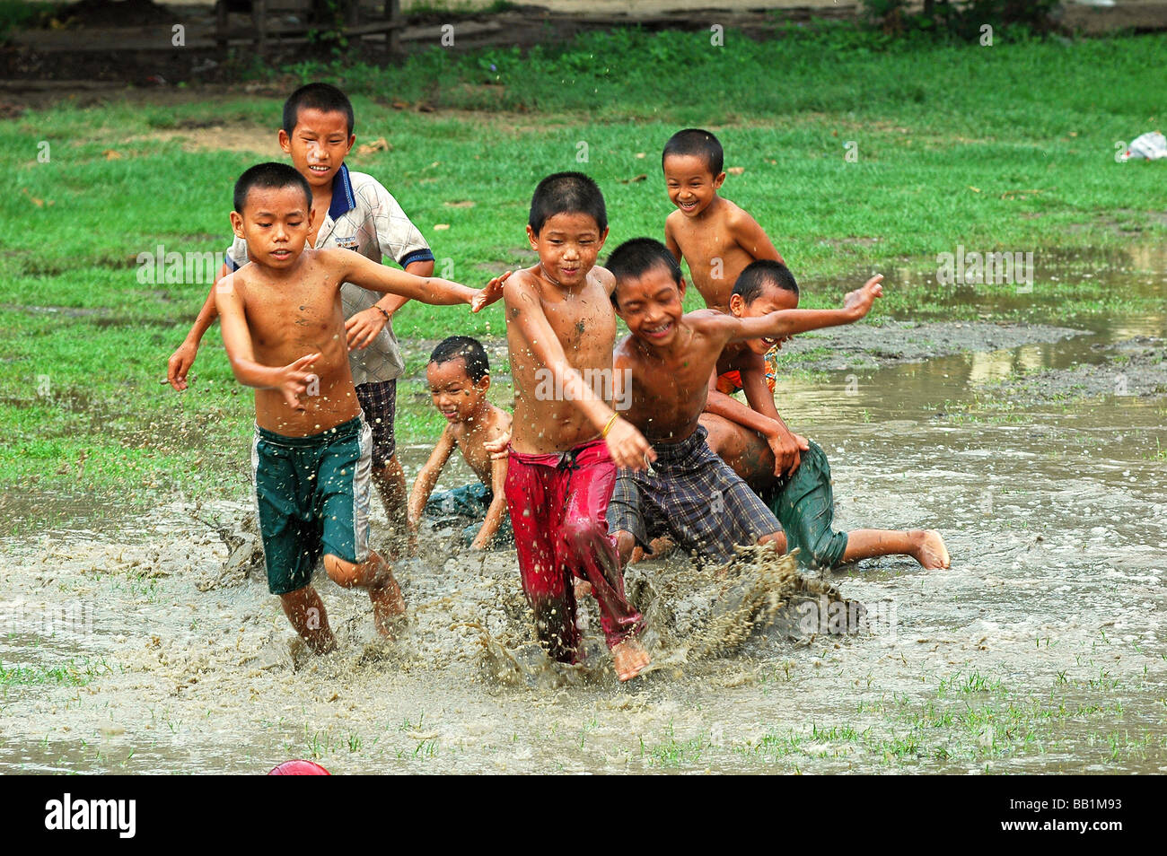 Le Myanmar, Mandalay. Garçons asiatiques course et le torse nu dans l'eau boueuse ponds Banque D'Images