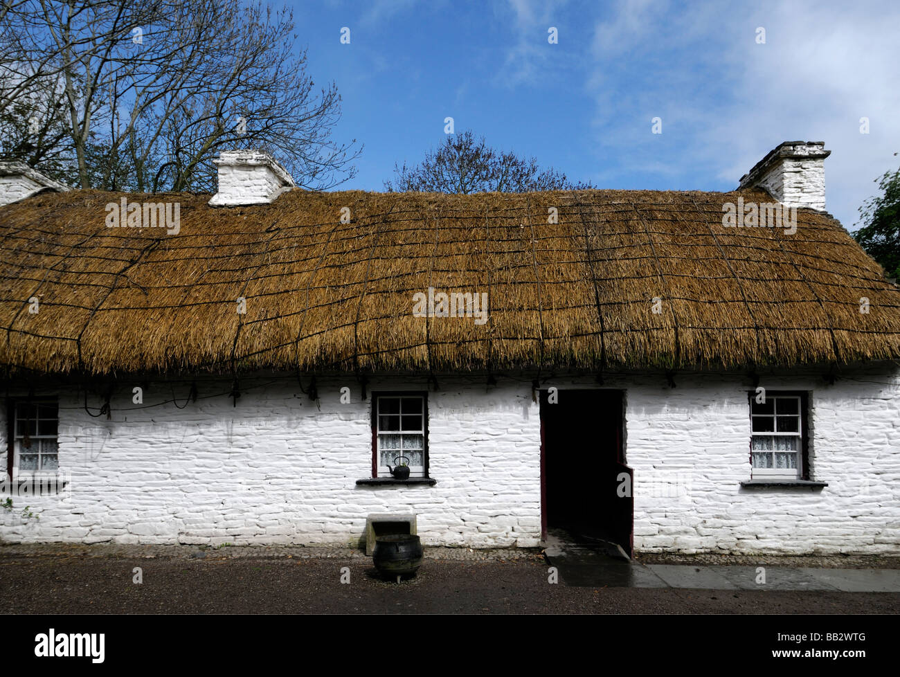 Cottage au toit de chaume avec porte en bois semi-ouverte de la fenêtre blanche maison traditionnelle en pierre peint en blanc ciel bleu l'Irlande Banque D'Images