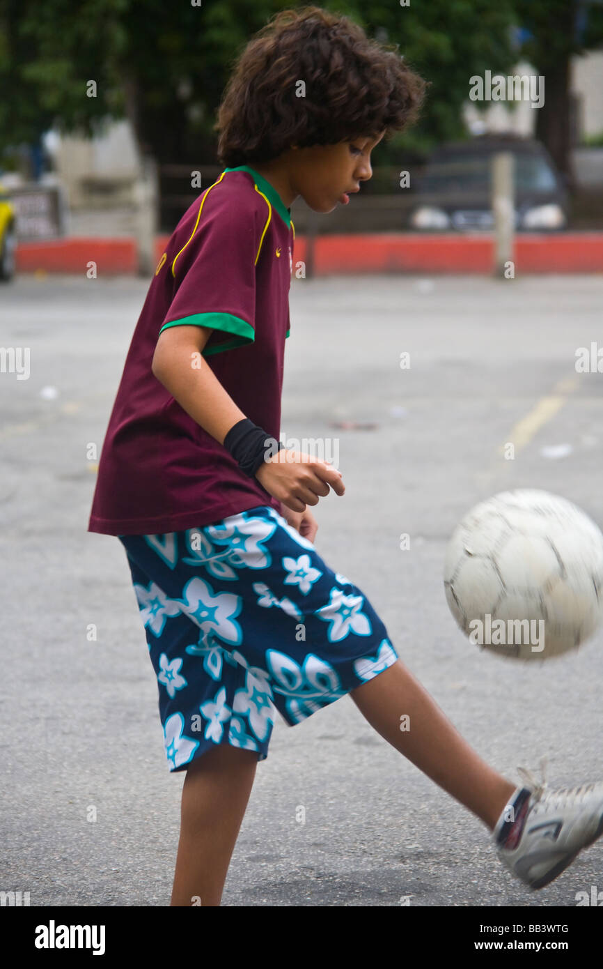 Jeune garçon brésilien jouant au football sur un terrain de stationnement à Rio de Janeiro, Brésil. Banque D'Images