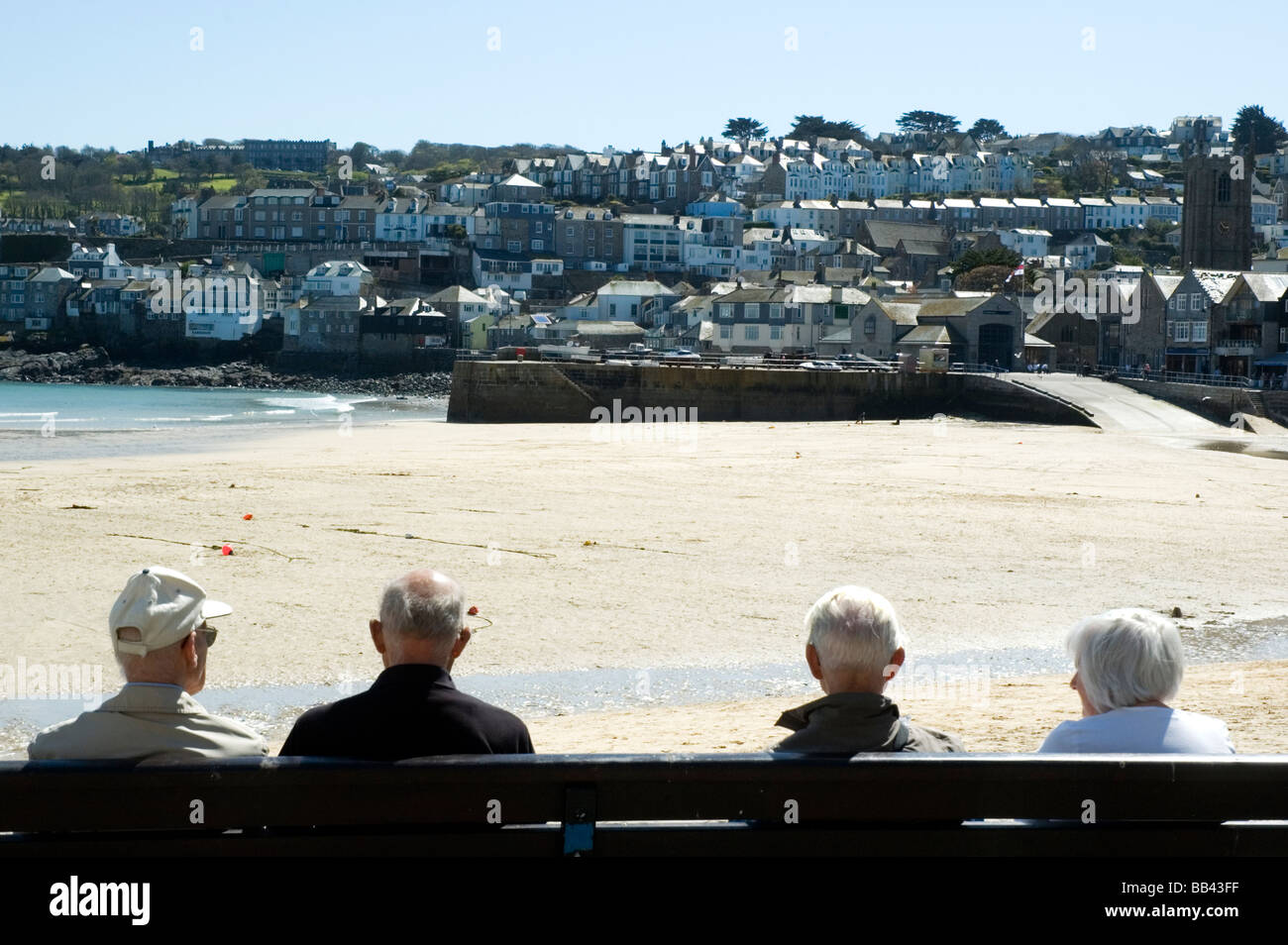 Quatre vieillards assis sur un banc au soleil donnant sur la plage à St Ives, Cornwall. Banque D'Images
