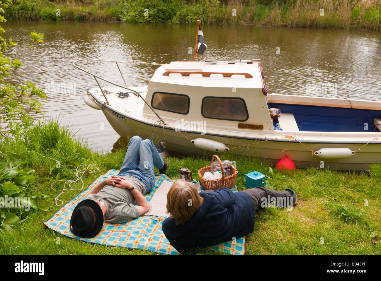 Un couple d'âge moyen bénéficiant d''un pique-nique au bord du fleuve à côté de leur bateau sur la rivière Waveney sur les Norfolk Broads au Royaume-Uni Banque D'Images