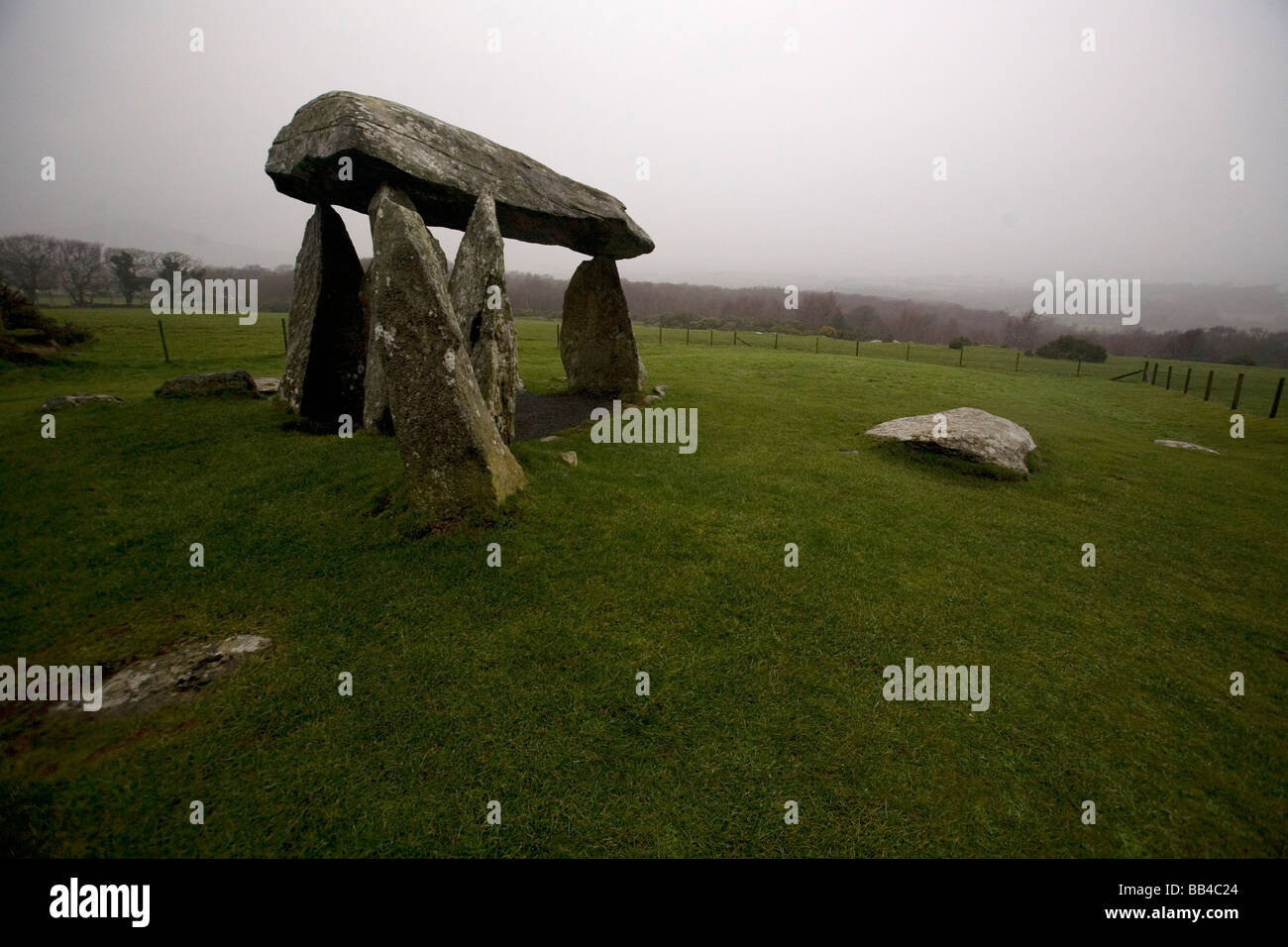 Pierre massive en équilibre sur d'autres pierres massives au milieu d'une herbe verte avec la pluie. Banque D'Images