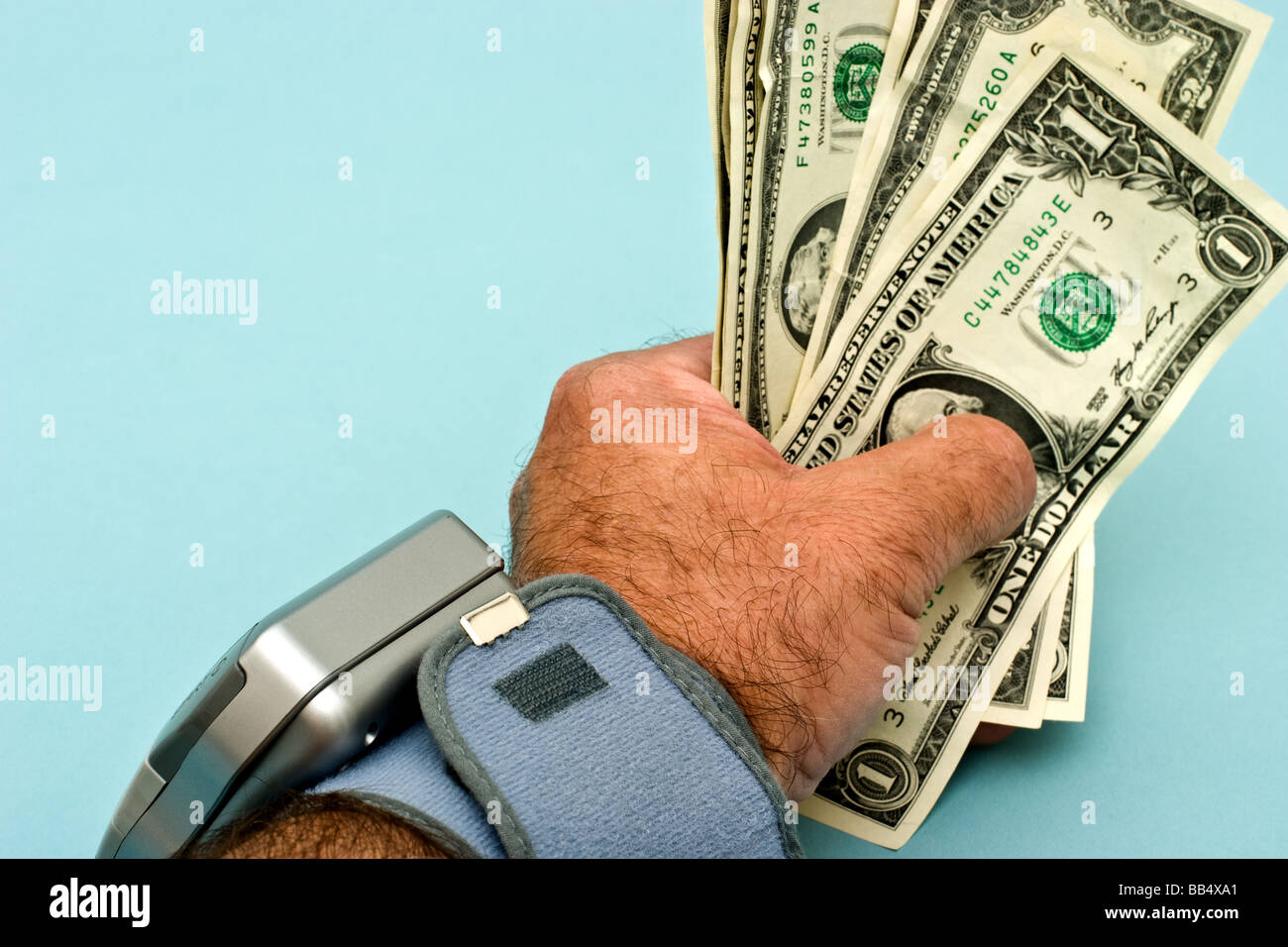 Man's hand holding American dollar bills avec un moniteur de pression sanguine sur son poignet Banque D'Images