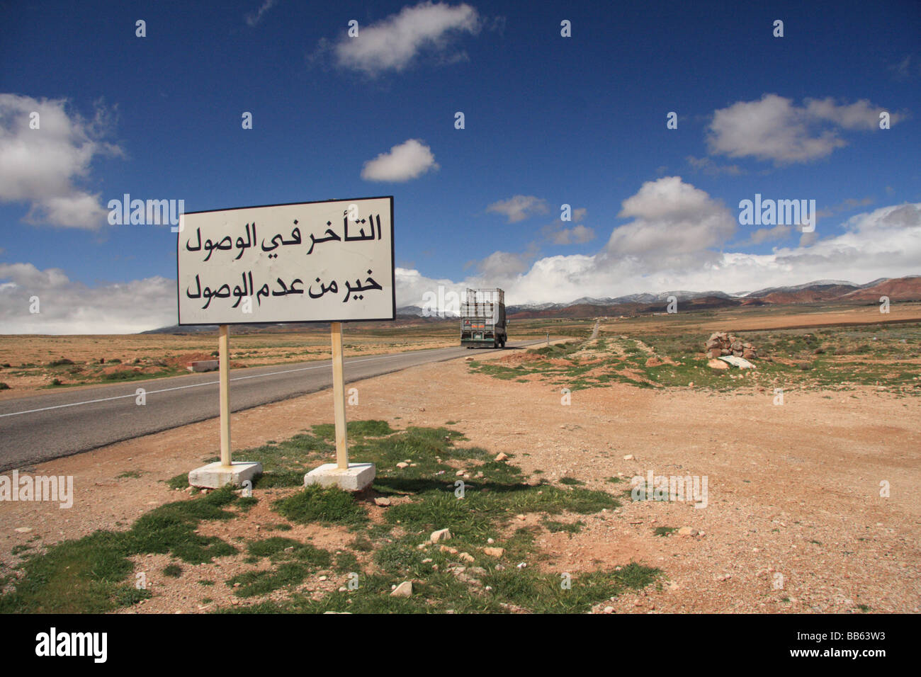 Panneau routier en arabe sur une route à travers le Moyen Atlas se lit comme suit : "mieux vaut arriver en retard que pas du tout' Ifrane, Maroc Banque D'Images