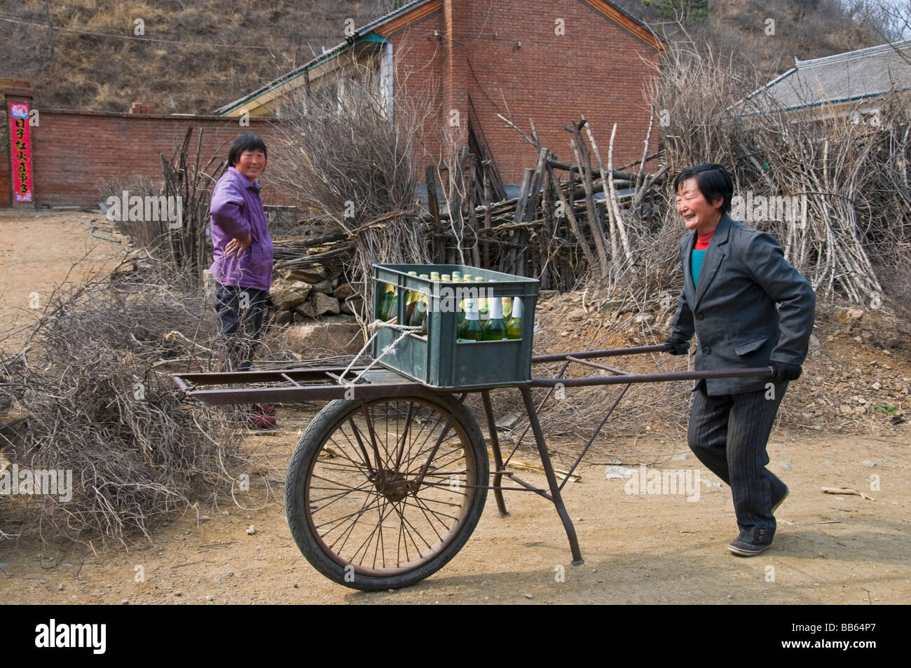 Une femme du village en poussant un panier de bouteille de bière en Chine rurale Banque D'Images