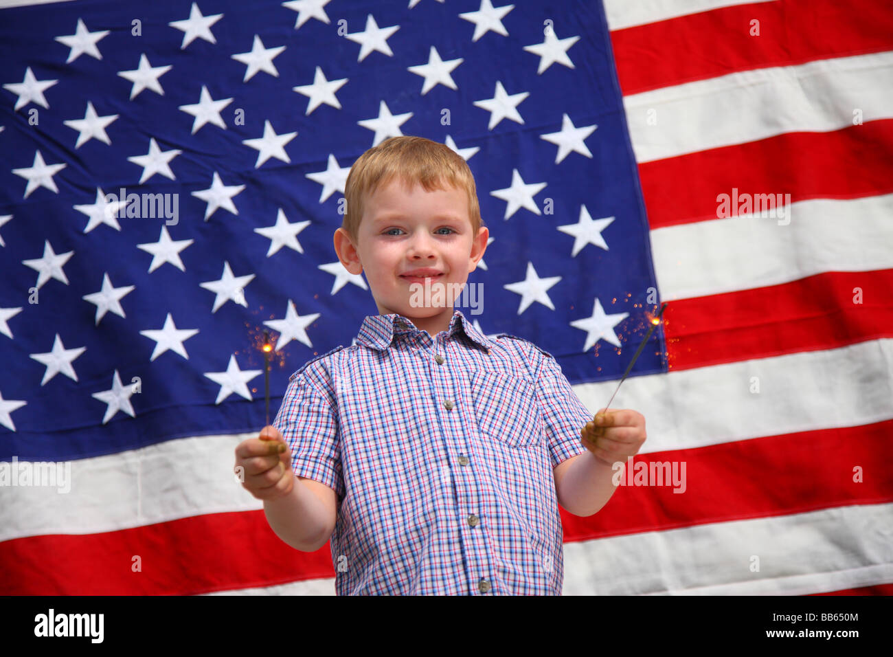 Jeune garçon waving sparklers in front of American flag Banque D'Images