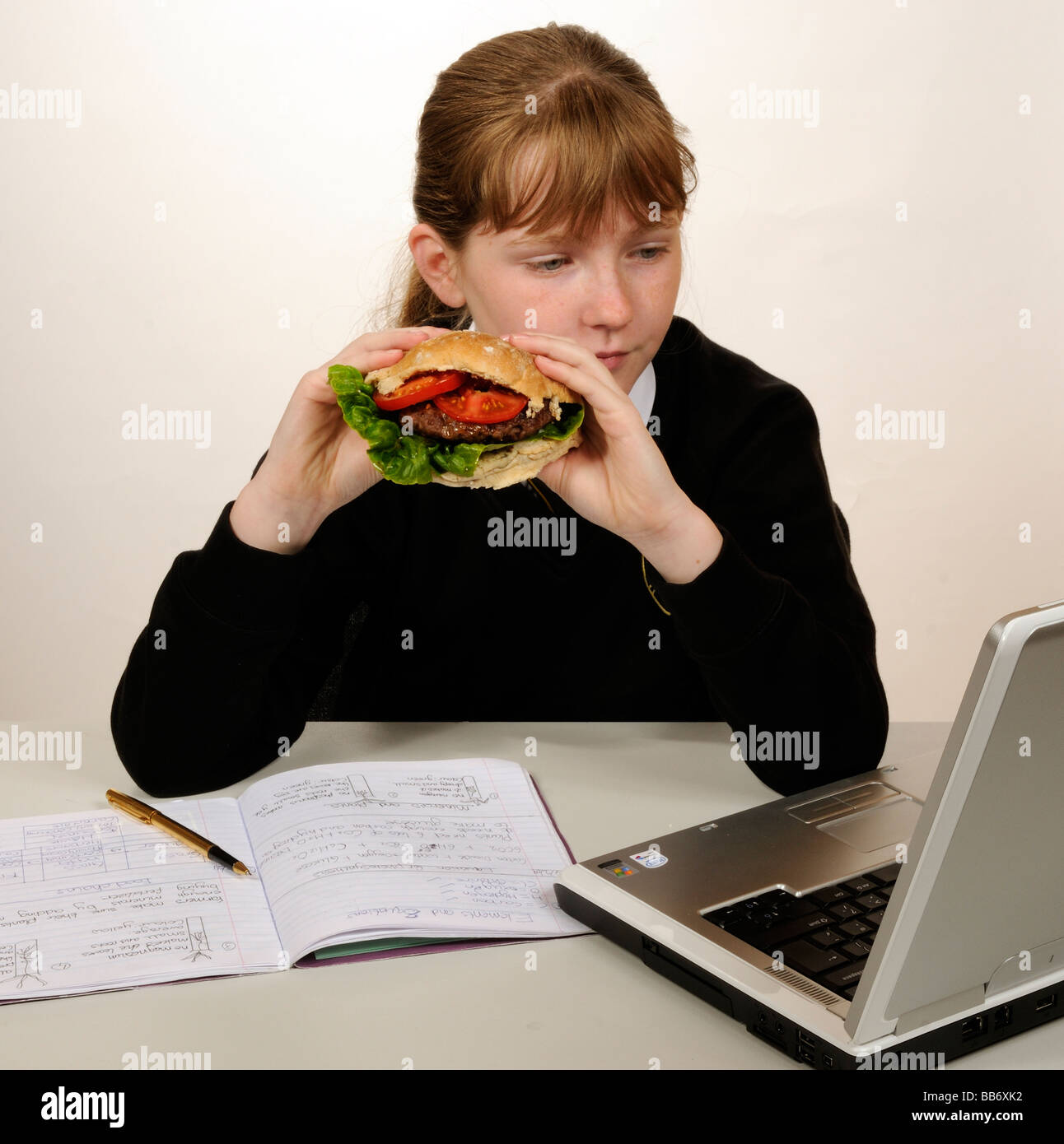 Manger une écolière beefburger avec une salade saine tout en faisant ses devoirs de remplissage Banque D'Images