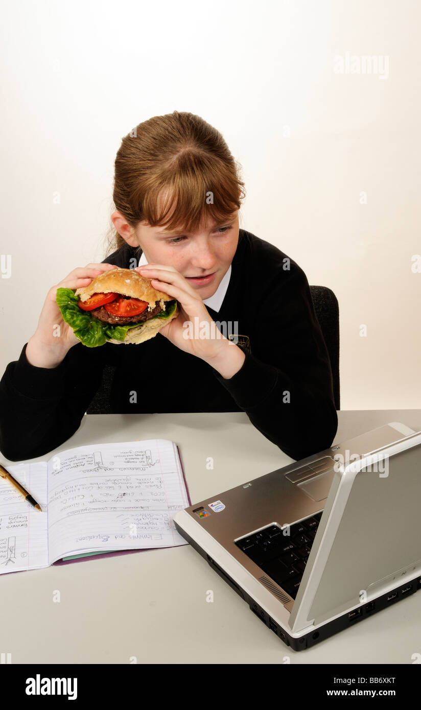 Manger une écolière beefburger avec une salade saine tout en faisant ses devoirs de remplissage Banque D'Images