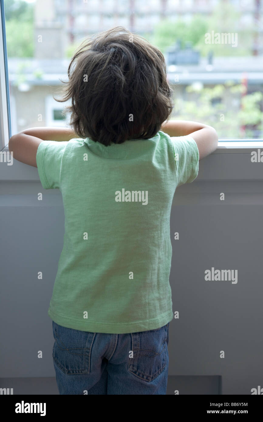 Un de petit garçon solitaire en regardant par la fenêtre Banque D'Images