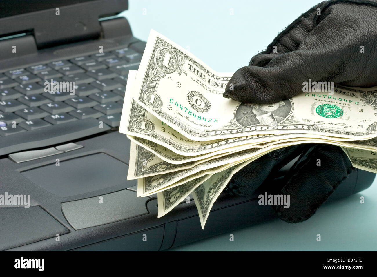 American dollar bills dans une main gantée sur un clavier d'ordinateur portable Banque D'Images