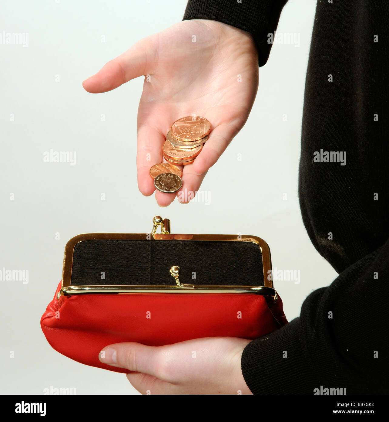 Enfant mettant de l'argent dans un sac à main rouge un cent et deux pièces pence Banque D'Images