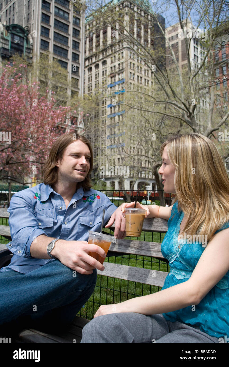 Un jeune couple assis sur un banc de parc avec des cafés glacés, Central Park, New York City Banque D'Images