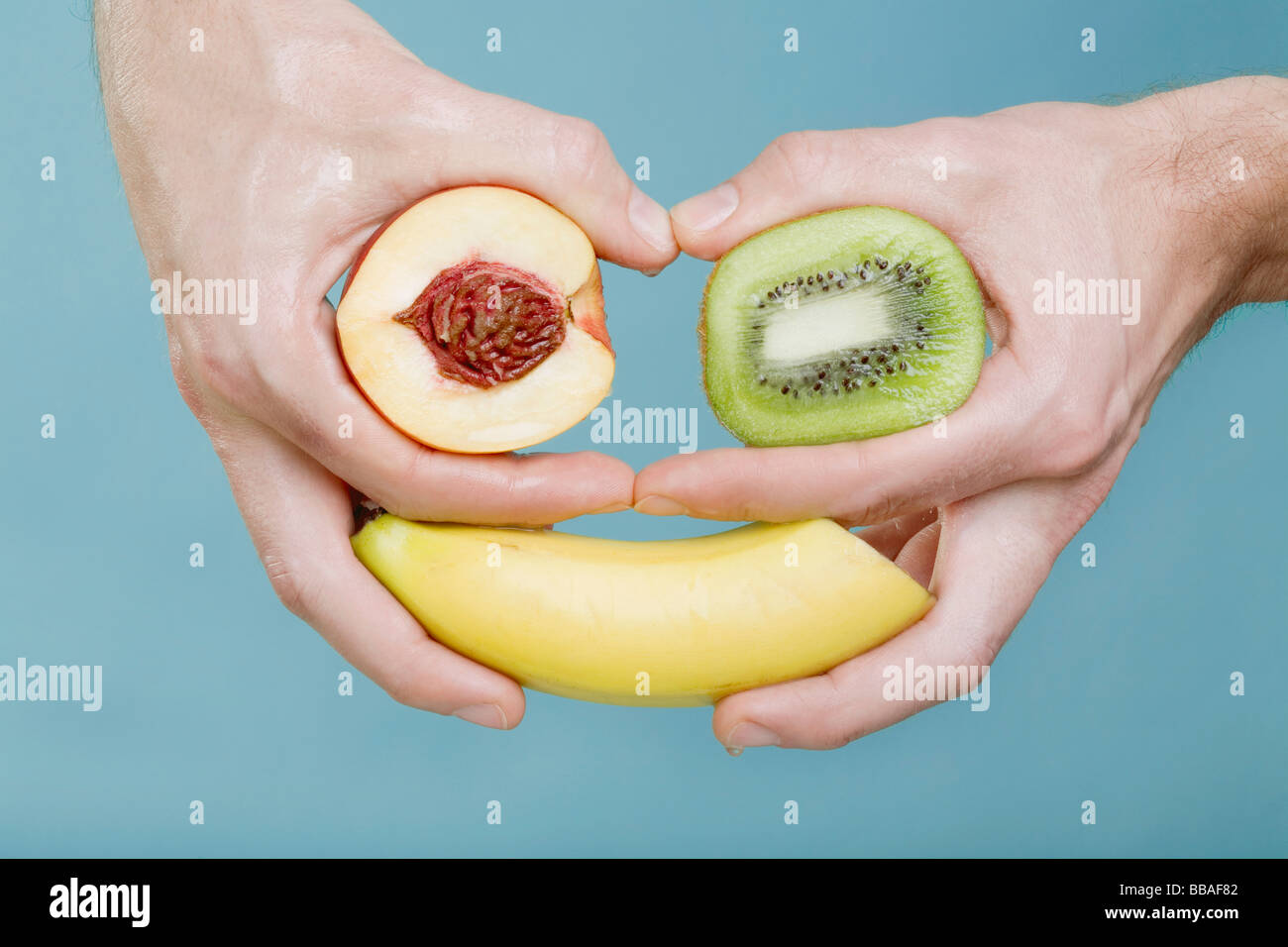 Les mains tenant des fruits dans un arrangement qui ressemble à un visage Banque D'Images