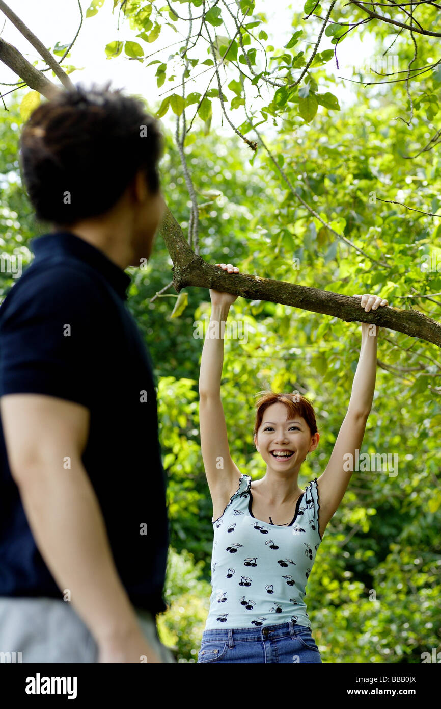 Femme accrochant sur branche d'arbre, à la recherche de l'homme en face d'elle Banque D'Images