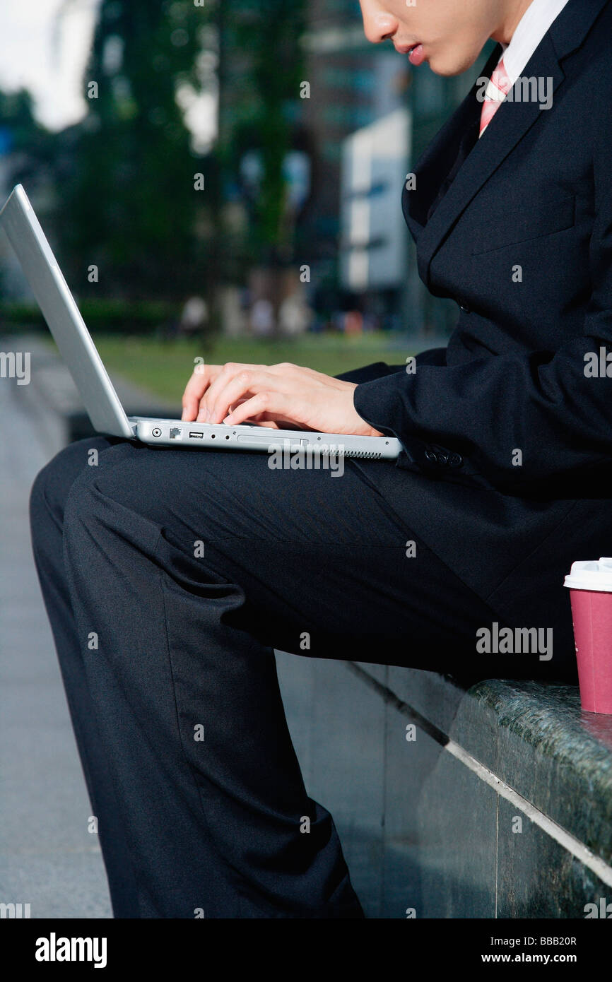 Un homme est assis et utilise son ordinateur portable à l'extérieur Banque D'Images